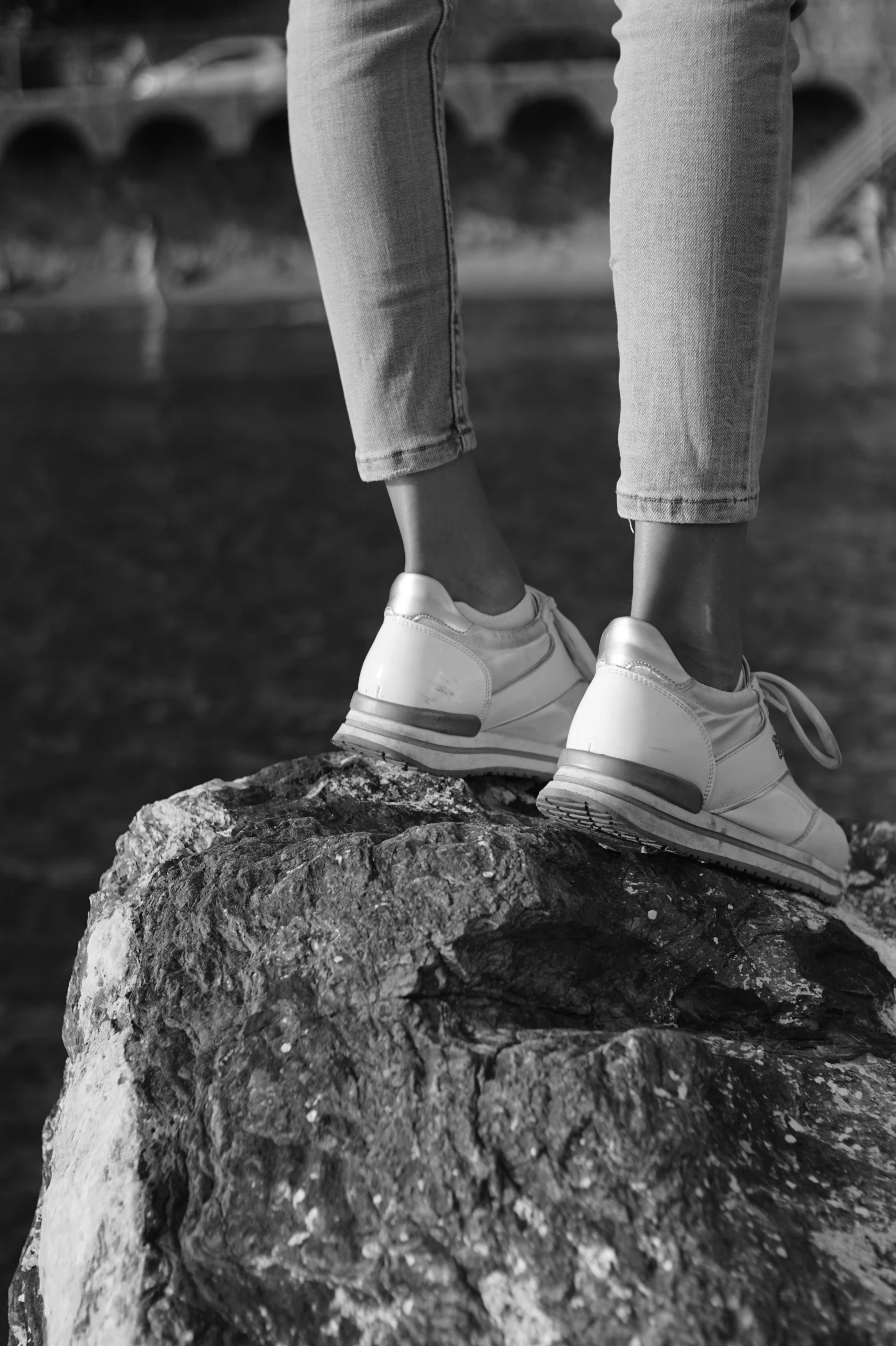 the foot of a person standing on the rock near a body of water