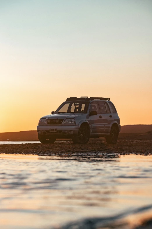 an suv sitting on the beach during sunset