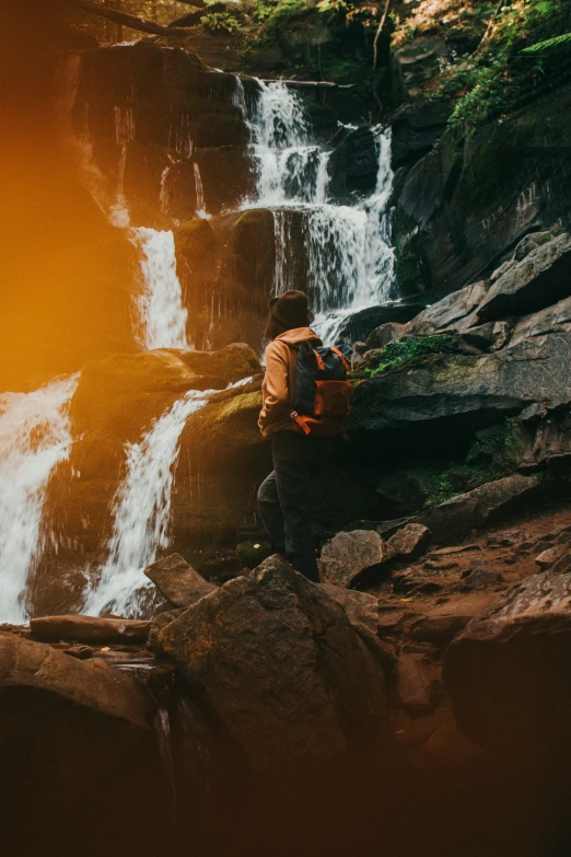 the hiker stands in front of the waterfall while he reaches for his backpack
