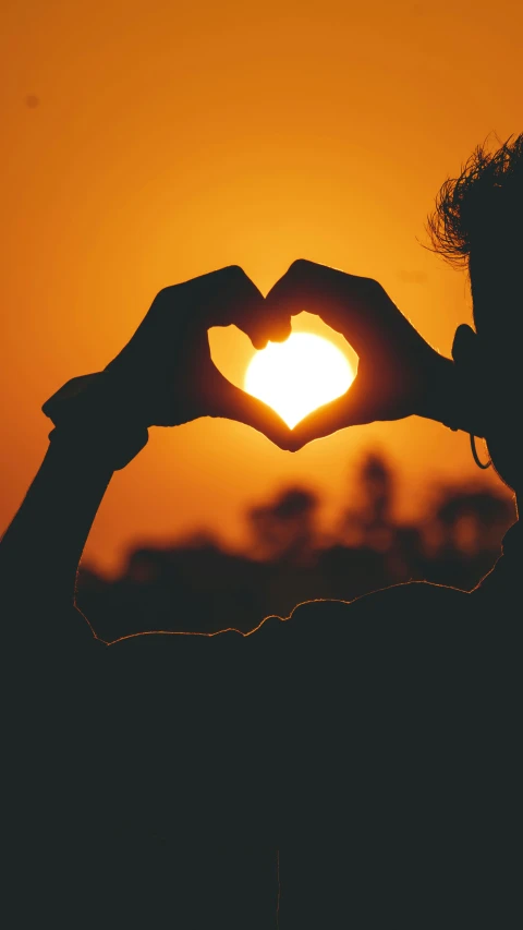 the silhouette of a person making a heart shape with their hand