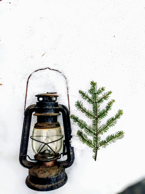 a small green nch sitting in the snow next to a lit lantern