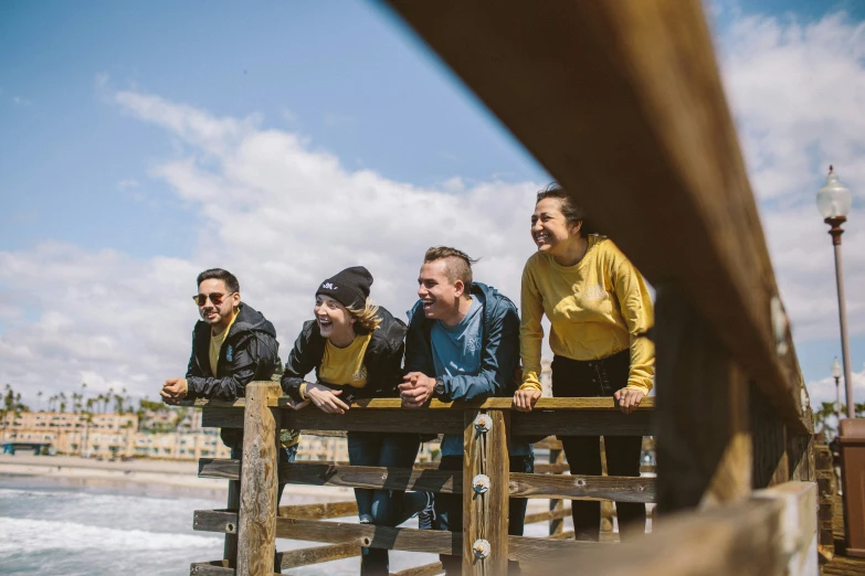 four people sitting on the wooden planks overlooking the ocean