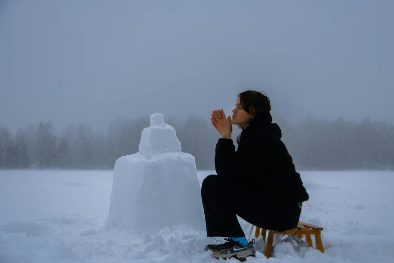 a young woman sits on a bench in front of a snow man