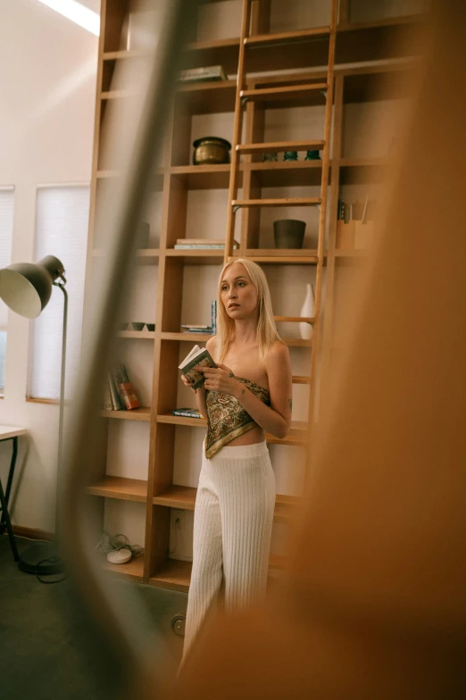 a beautiful blonde girl standing in a room near a bookshelf