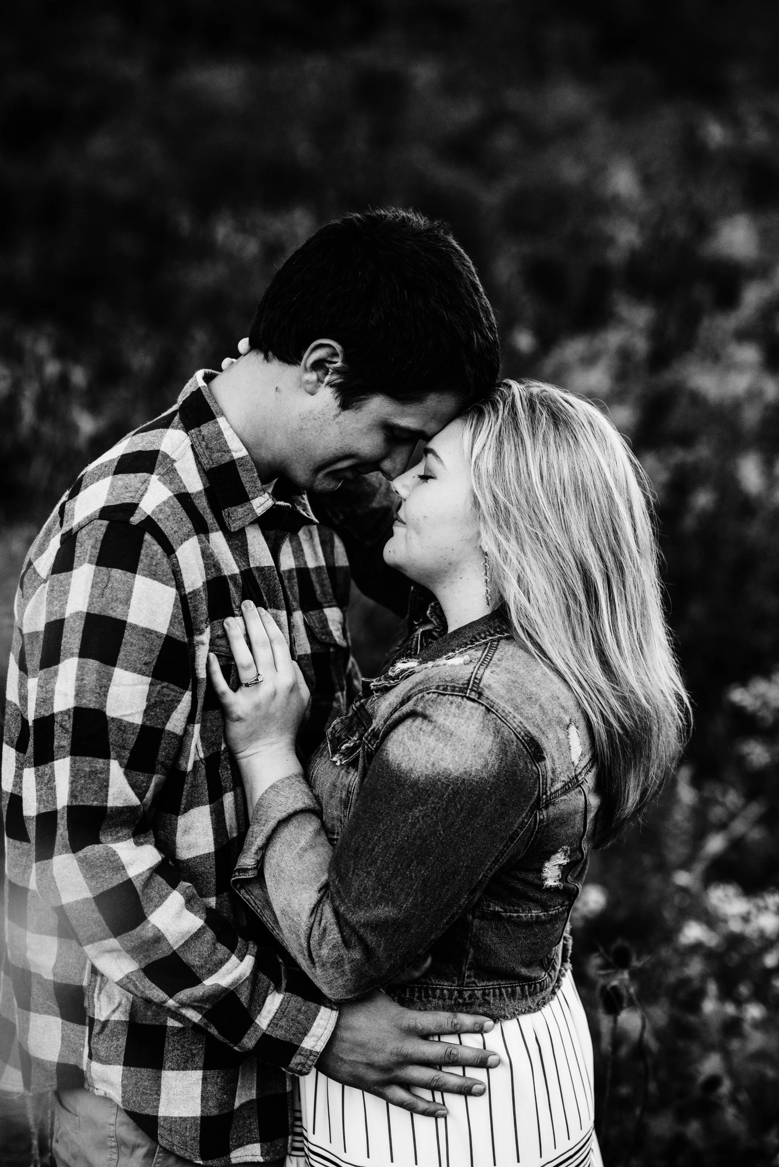 a woman hugs her man while they kiss in an open field