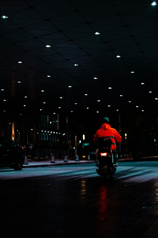 a motorcycle rider wearing red rides down a street at night