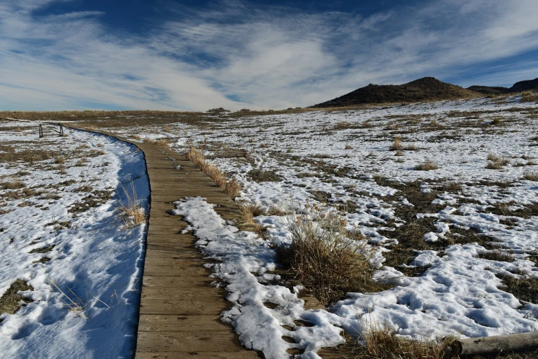 a pathway with snow on the ground in front of mountains