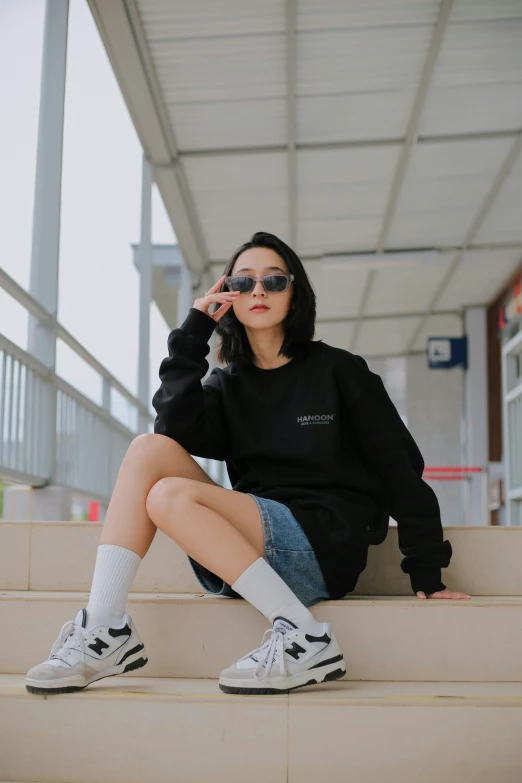 an asian woman in a black sweatshirt is sitting on steps with white shoes and a black beanie