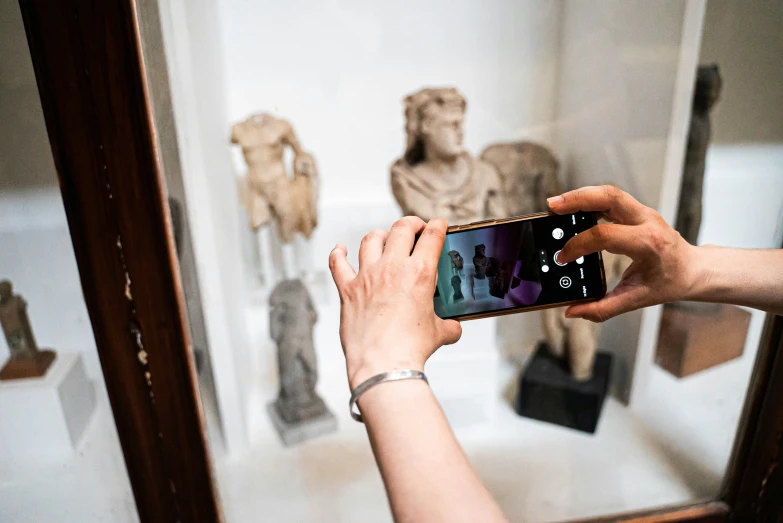 someone taking a po with their phone of an ancient statue behind a glass case