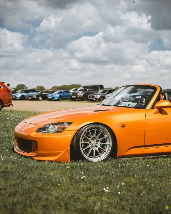 a large orange convertible sits on a field near cars