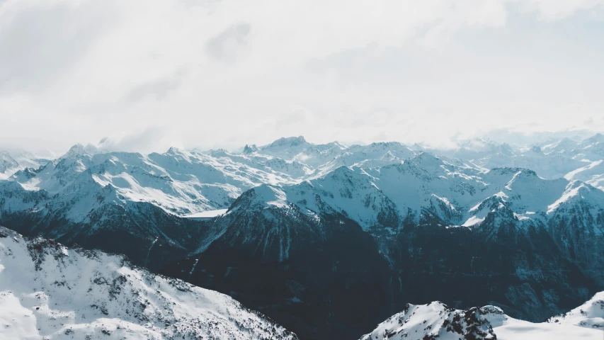 the mountains range are covered with snow and clouds