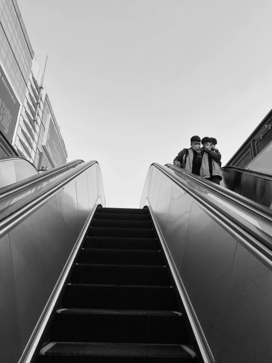 two people are going down an escalator towards a building