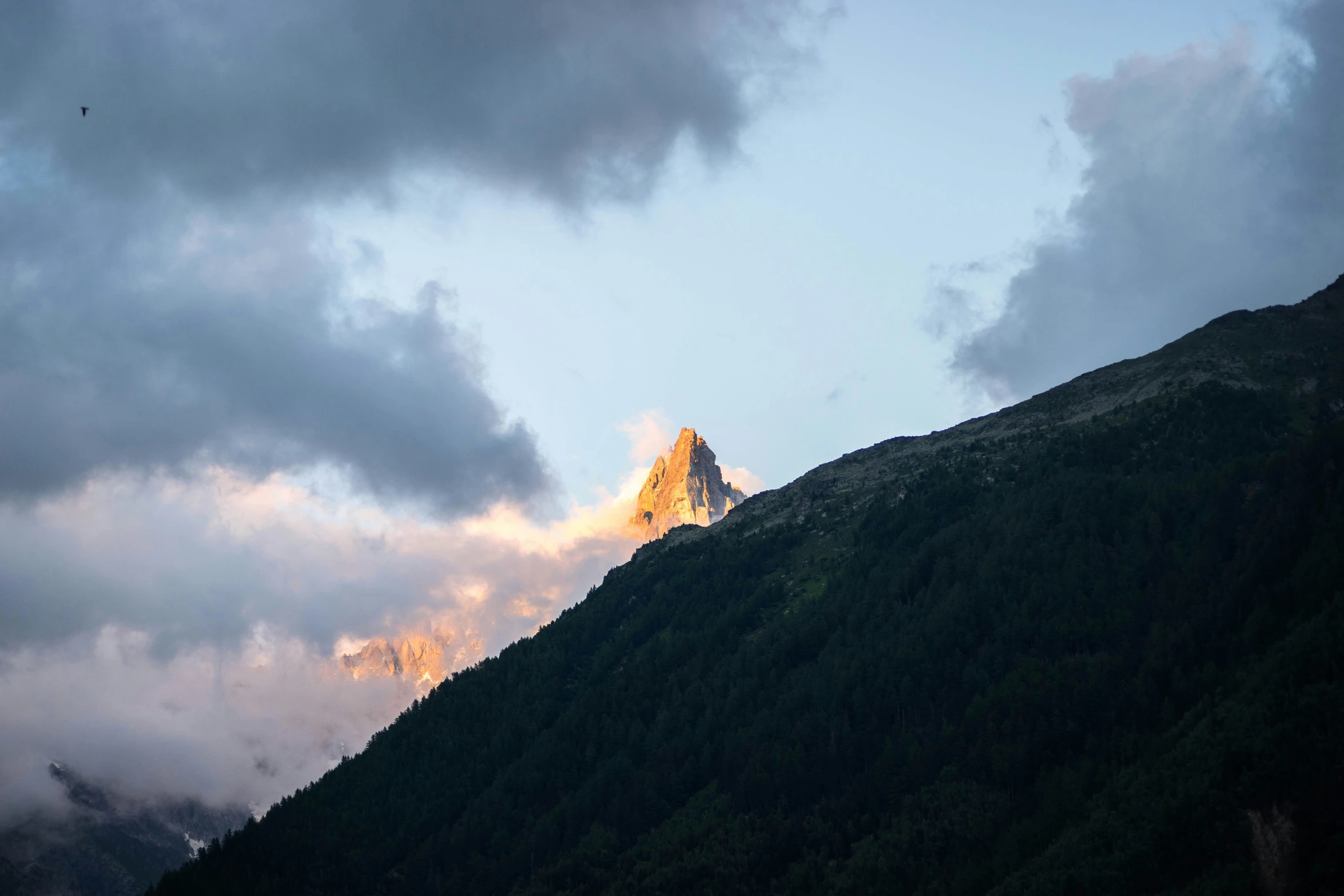 the peak of a mountain with clouds and blue sky in the background