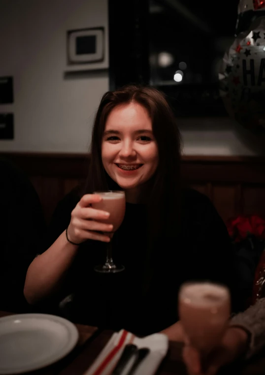 girl smiling holding up a glass at table