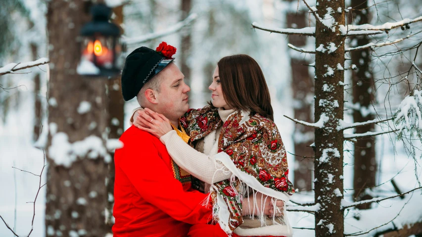 the couple stands in front of the tree in winter