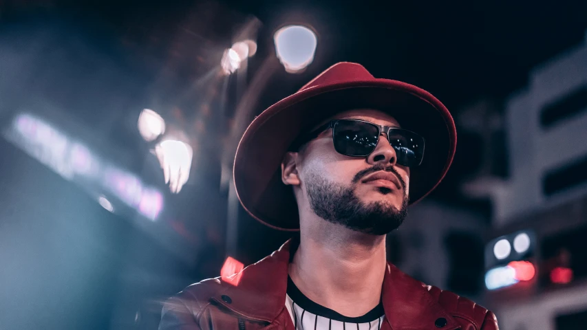 man wearing sunglasses and hat standing at night in the city