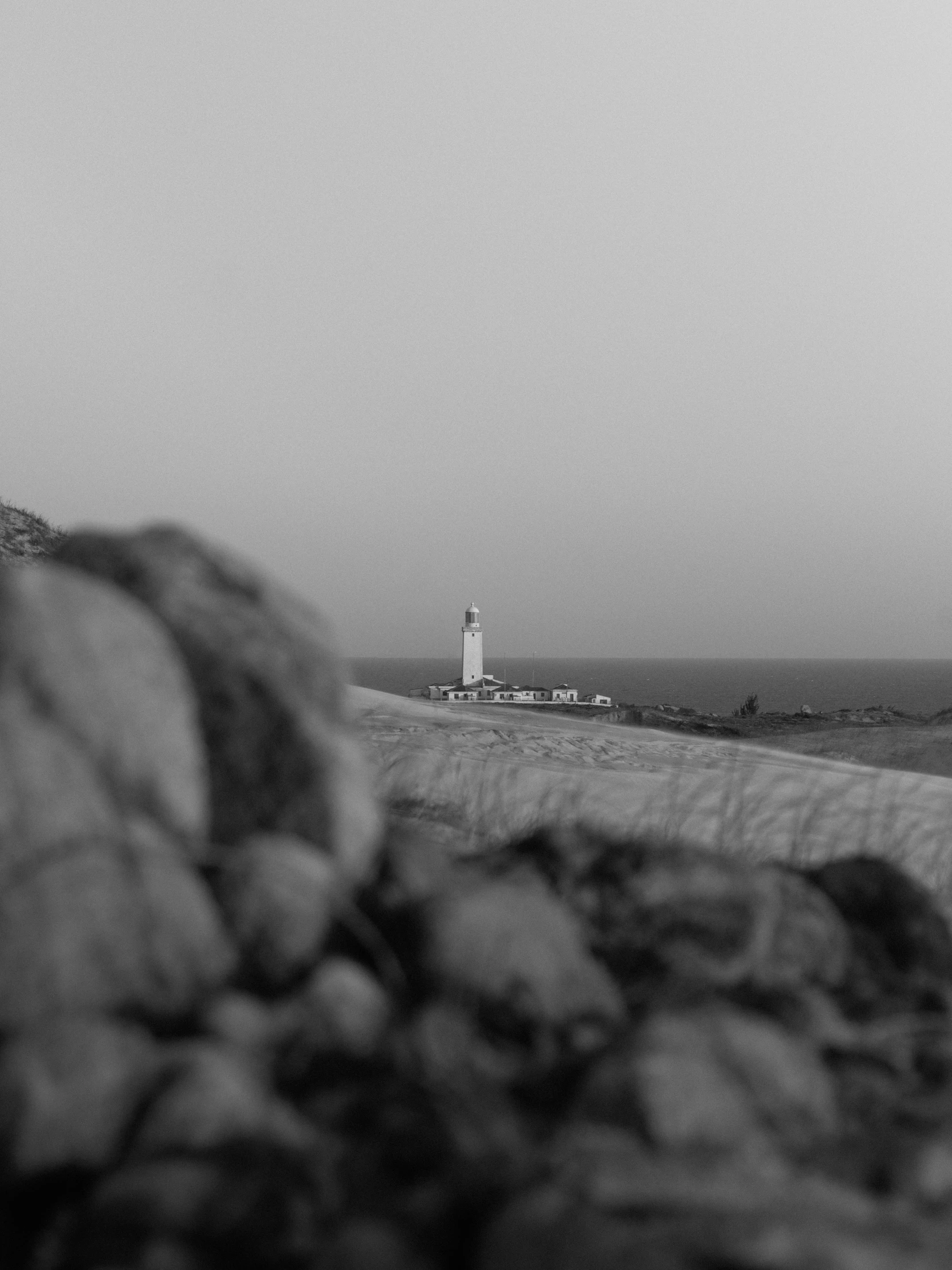 black and white pograph of lighthouse on rocky beach