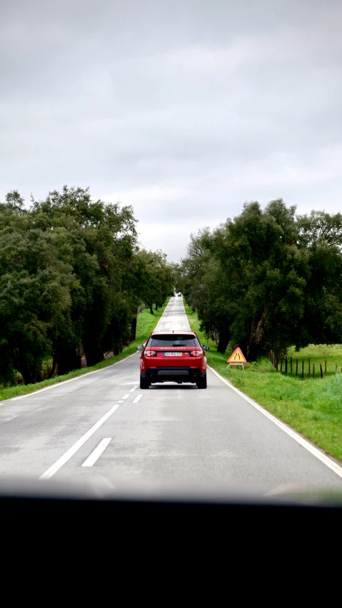 a red car is driving down a long road