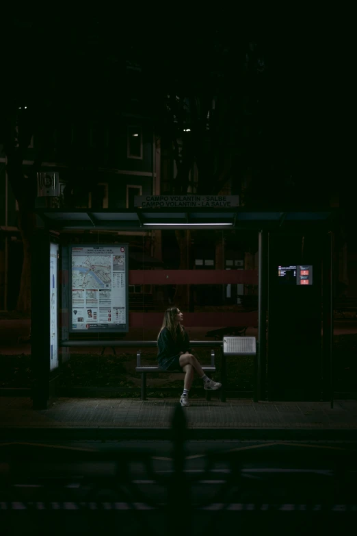 a woman is sitting on a bench at night