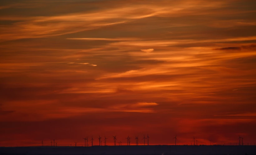 a sunset view of an oilfield with some wind generators in the background