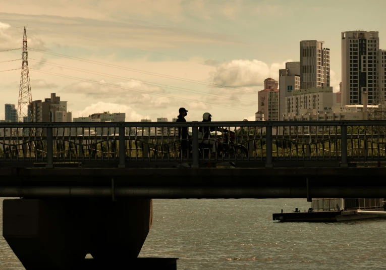 silhouettes of two people standing on a bridge next to a river