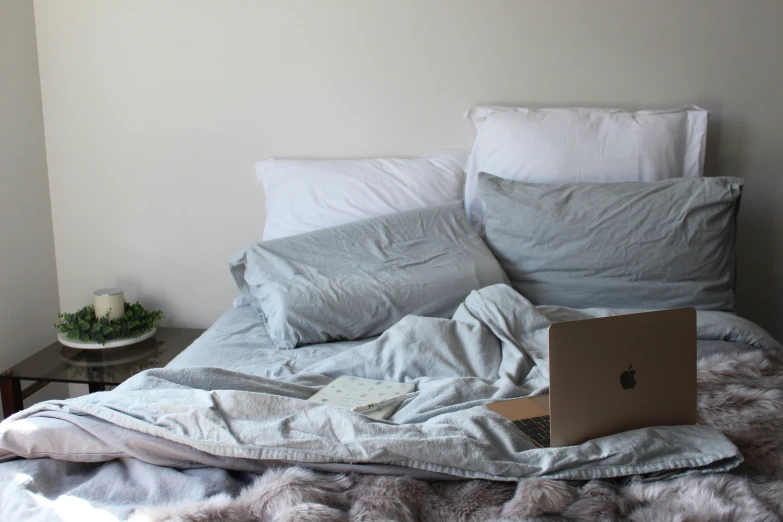 an apple laptop sits on a bed covered in blankets