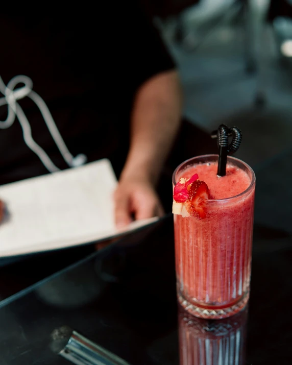 a red drink with strawberries sits on a black table