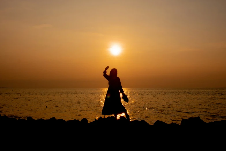 the silhouette of a woman standing on rocks, in front of a sunset