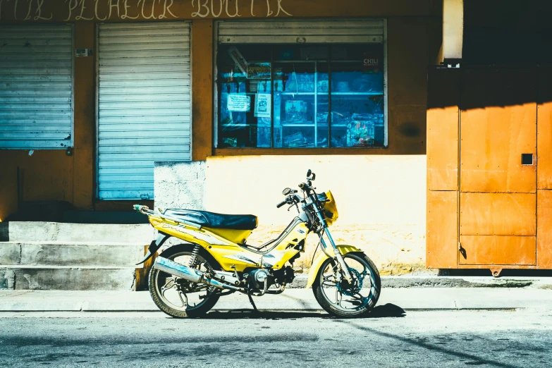 the yellow motorbike is parked on the sidewalk