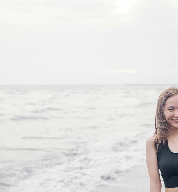 an attractive young lady standing on top of a beach near the ocean