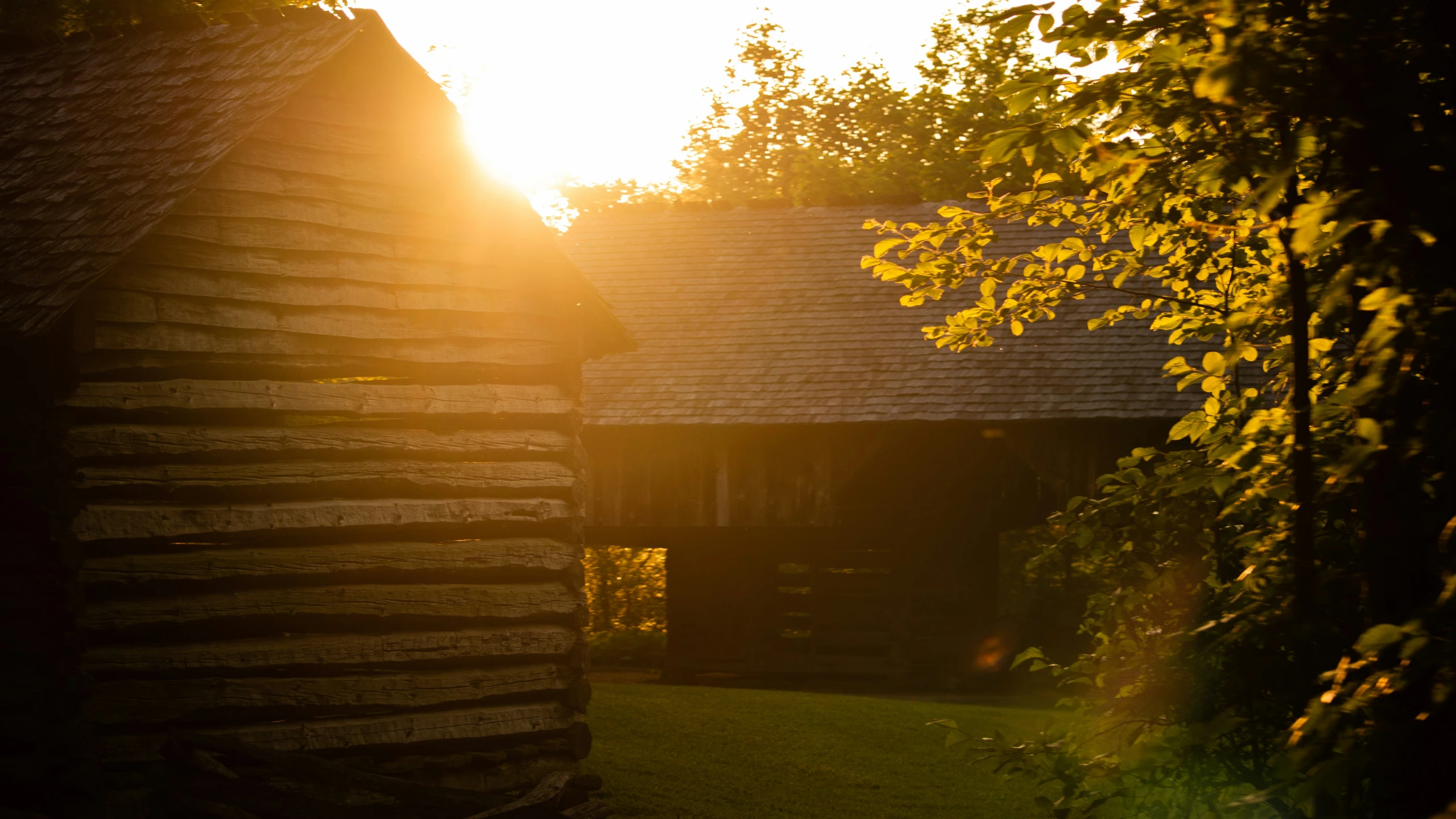 a barn with a wooden roof and a sun in the distance