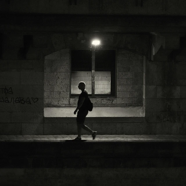 a dark street with a person walking on the sidewalk near a window