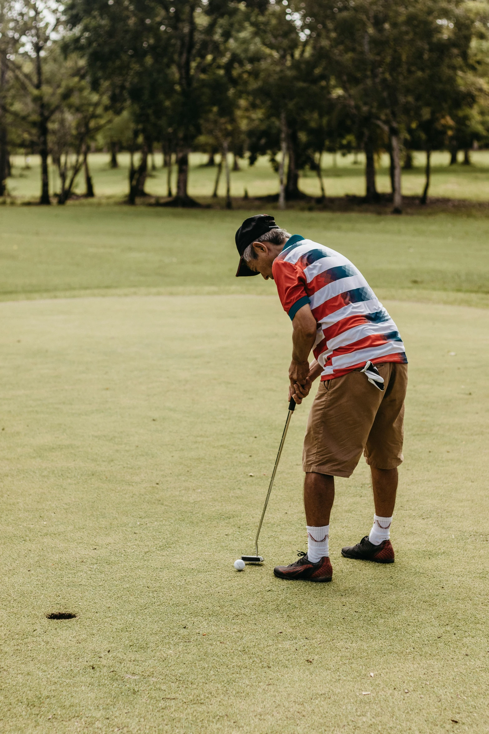 a man in shorts and striped shirt holding a golf ball on a green