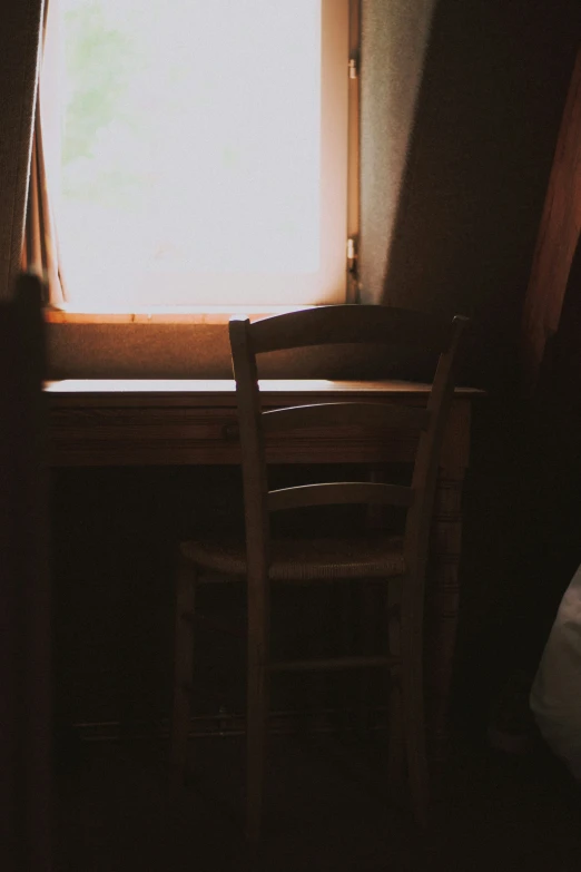 a chair and a table sit in a small room, lit up by the window