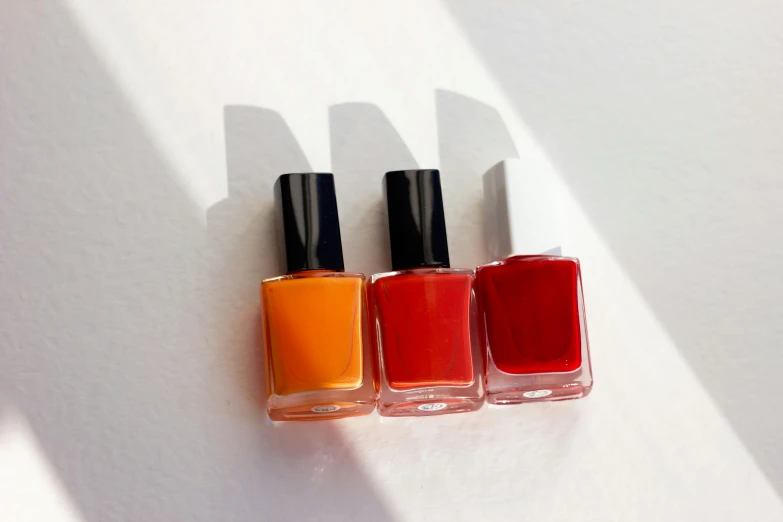 three orange and red nail polishes in three shades