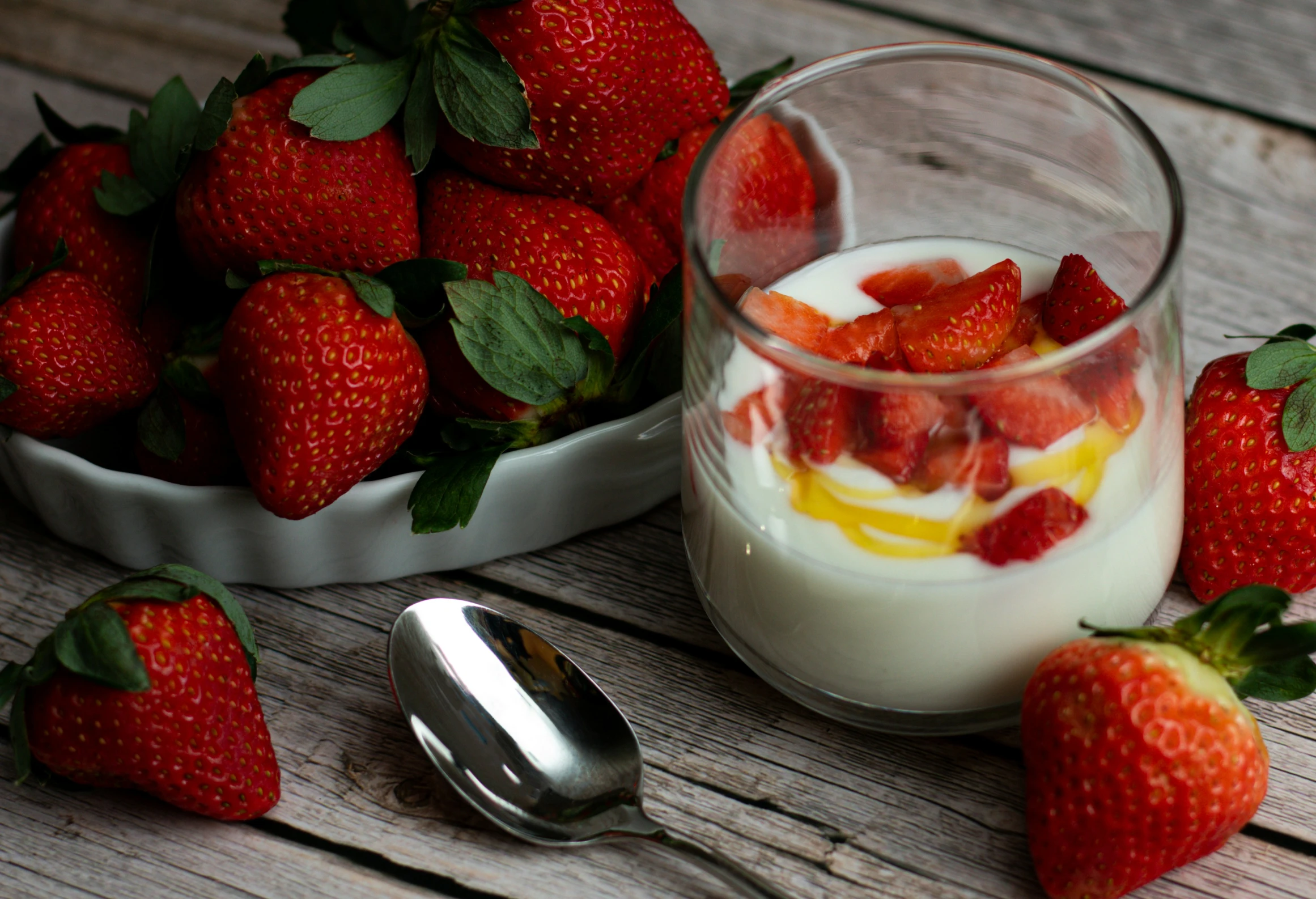 a glass cup filled with yogurt and strawberries next to bowl of berries