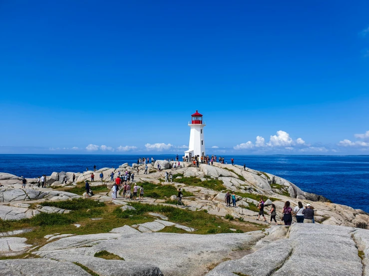 a crowd of people standing on a rock with a light house