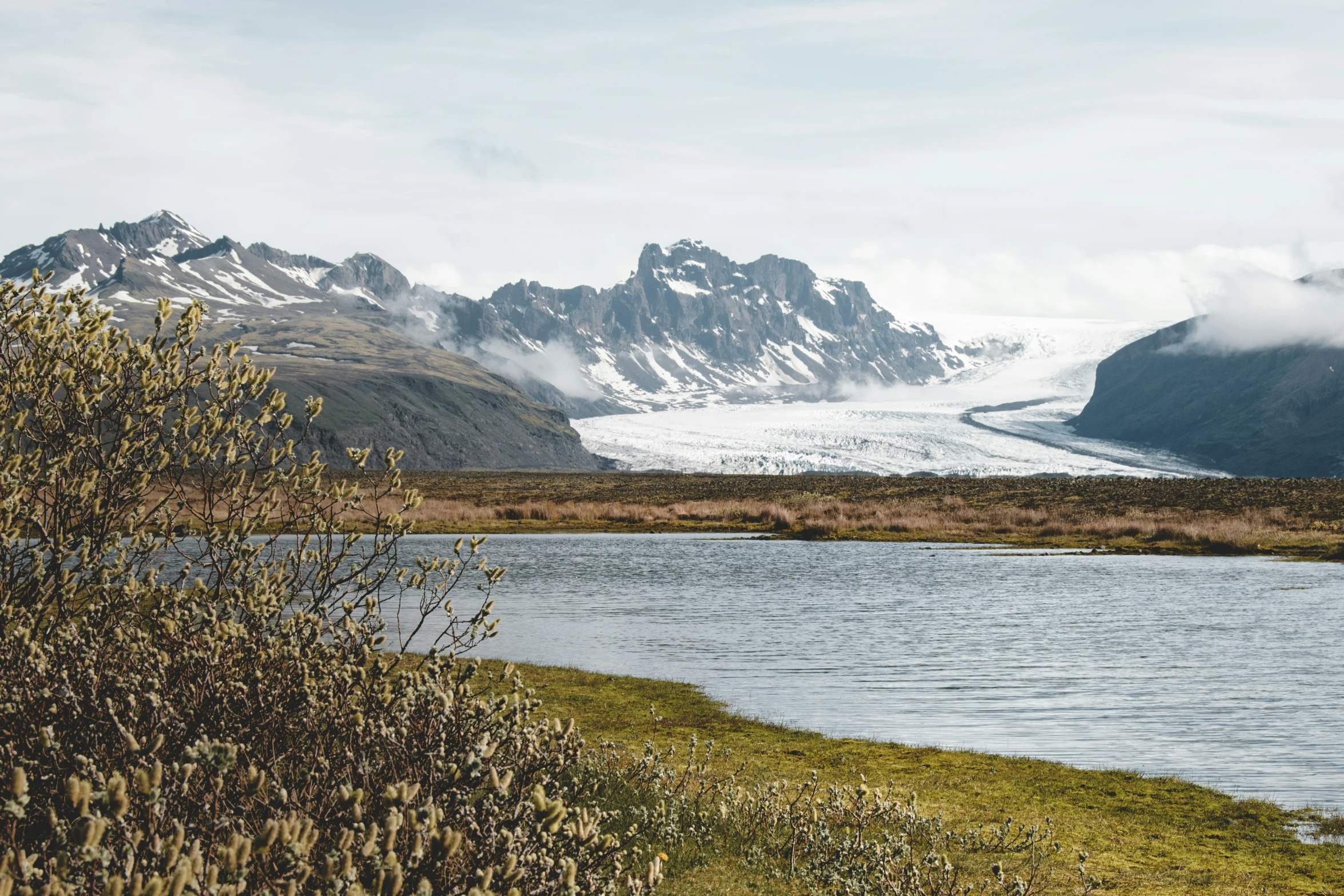 a body of water surrounded by grass and mountains