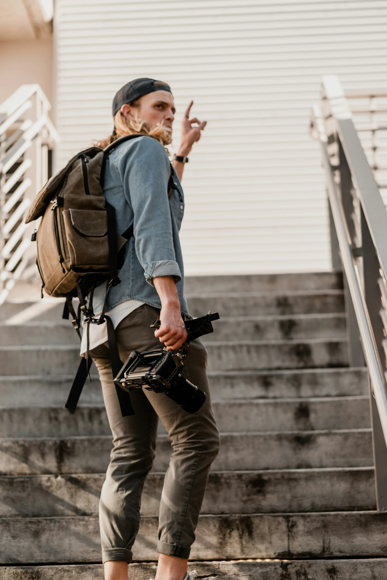 the man with a backpack and camera bags walks down some stairs