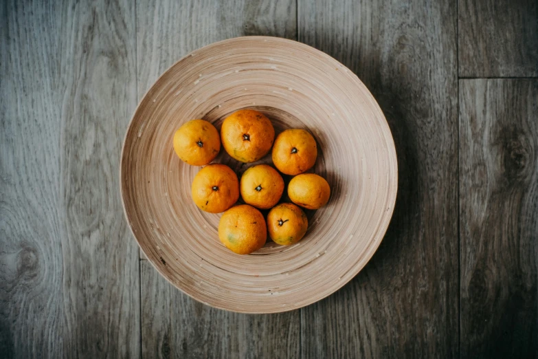 a wooden bowl full of oranges on top of a wooden table