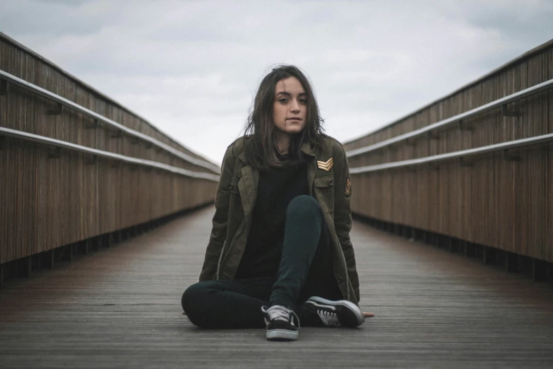 a young woman sitting on the floor in front of a bridge