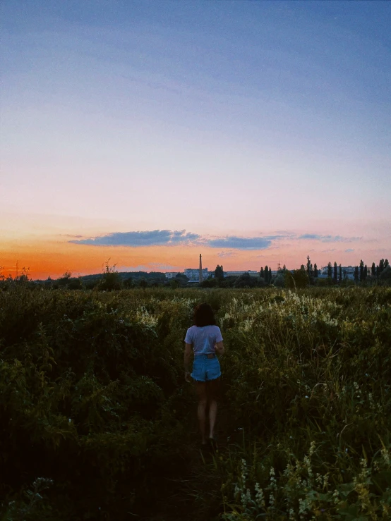 a girl standing in the middle of a field at sunset