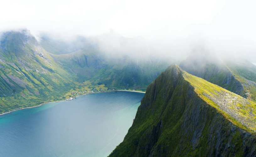 mountains and valleys covered with fog and mist next to a large body of water