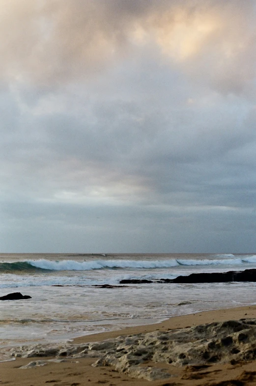 surfers on the beach under grey skies and crashing waves