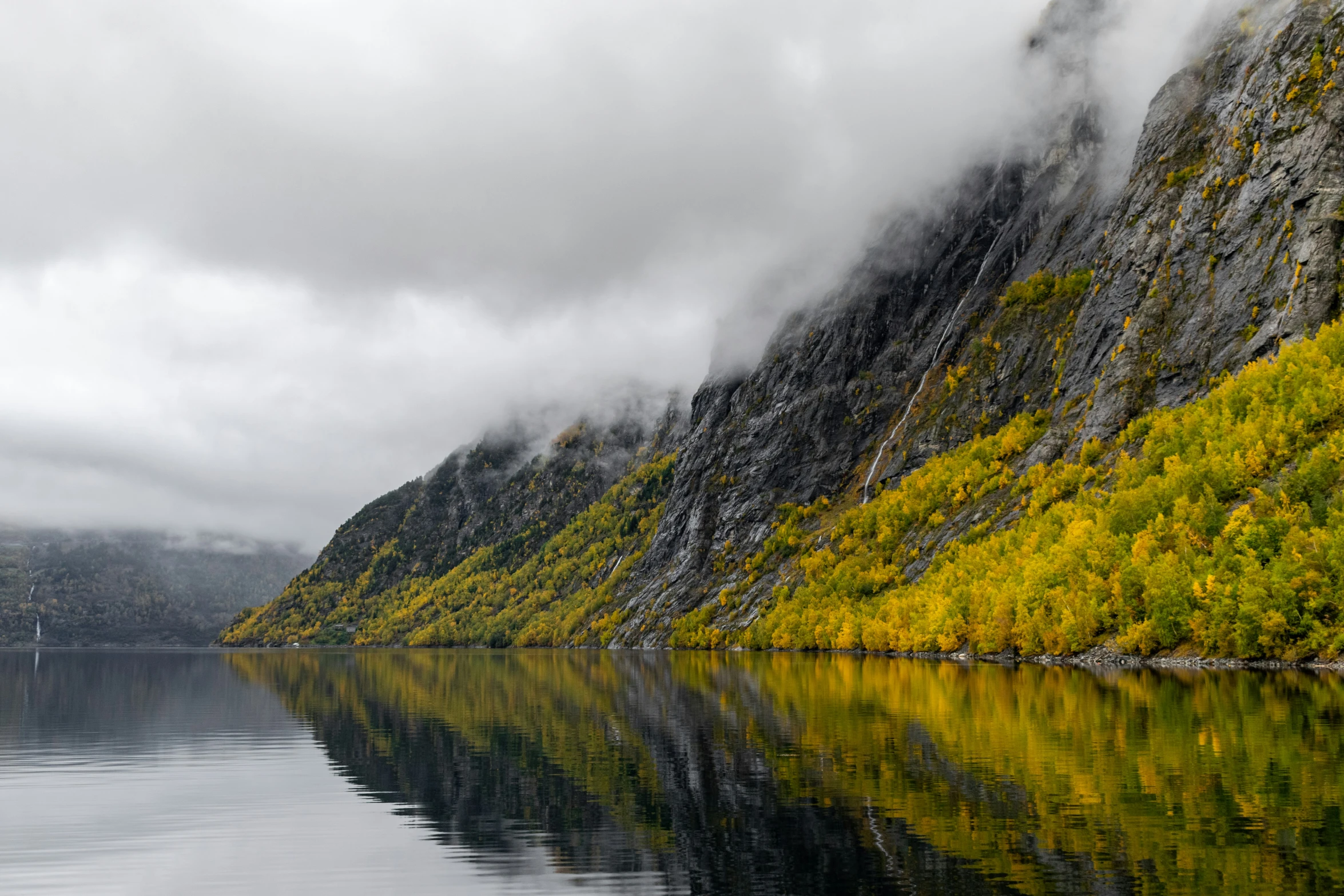 some mountains near the water with trees reflecting in it