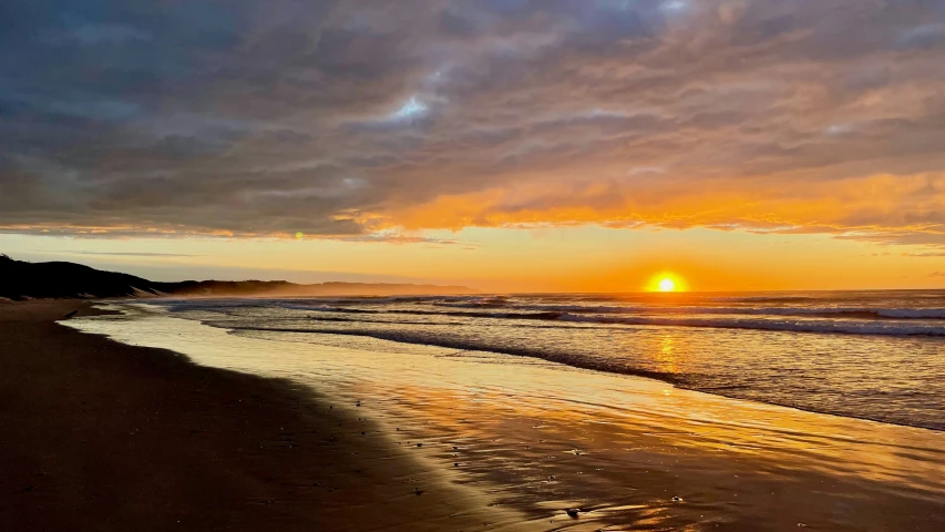 the sun is setting on the water at a beach