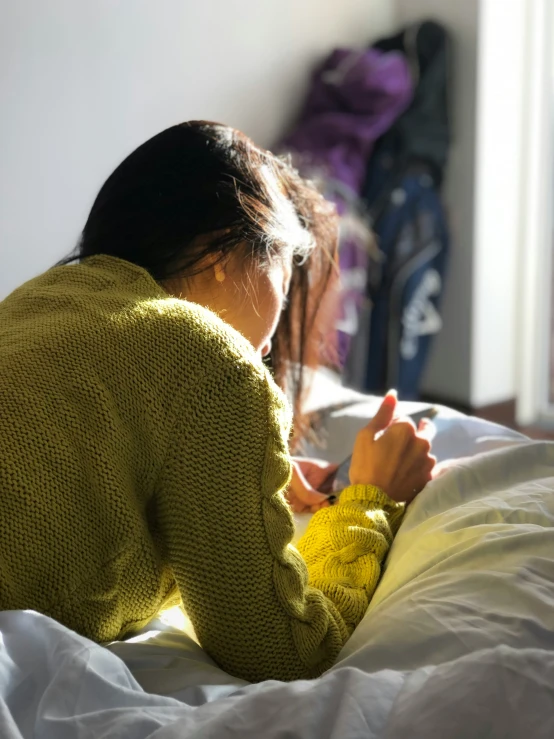 a young lady sitting on a bed looking at her phone