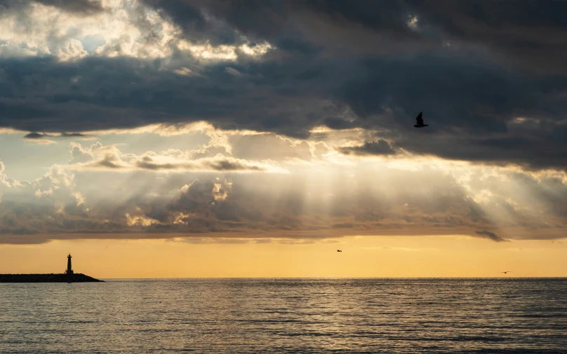 the clouds are above the ocean and a light house in the distance