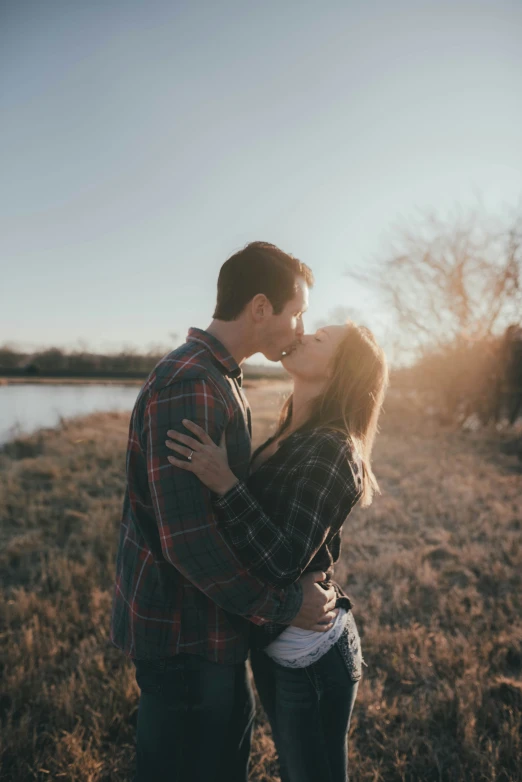 a beautiful couple sharing a kiss in a field near the water