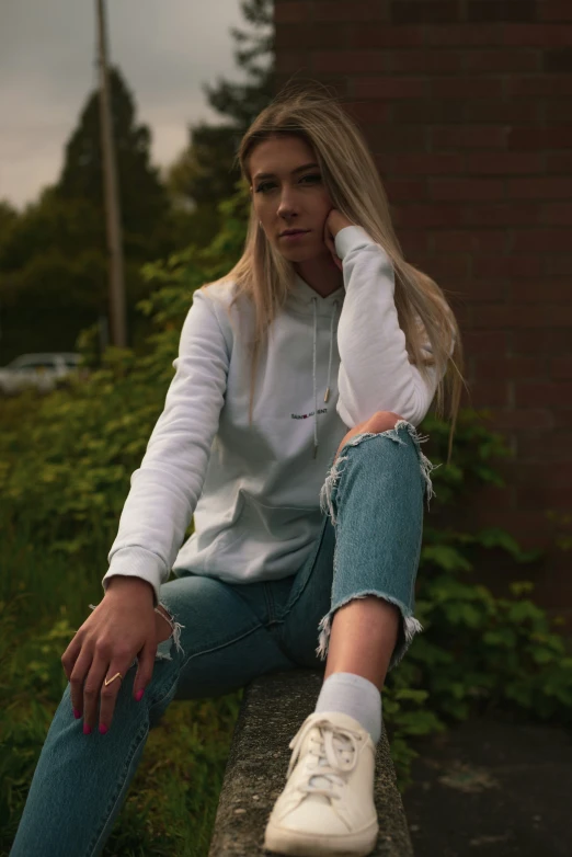 a woman is sitting down wearing jeans and a sweatshirt
